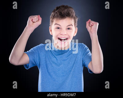 Émotionnel de mi-longueur portrait of caucasian teen boy. Adolescent crier victoire portant des T-shirt bleu sur fond noir. L'enfant gagnant drôle de crier Banque D'Images