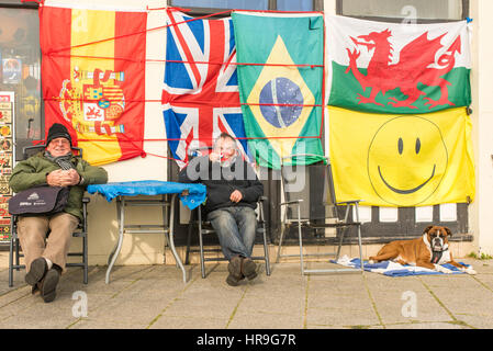 Deux hommes assis ensemble tasses de thé potable à l'extérieur d'un magasin qui vend des drapeaux sur le front de mer de Ramsgate, Kent. Banque D'Images