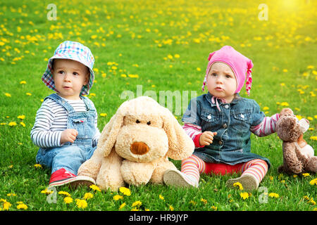 Petit garçon et fille en chapeau assis sur le terrain avec des jouets mous en été Banque D'Images