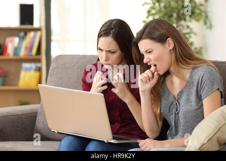Deux amis en colère médias regarder en ligne avec un pc assis sur un canapé dans la salle de séjour à la maison Banque D'Images