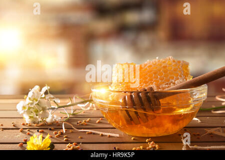 Bol avec le miel, miel et balancier sur une table en bois avec des fleurs et du pollen d'abeille dans une cuisine rustique avec sunbeam. Vue de face. Compositi horizontale Banque D'Images