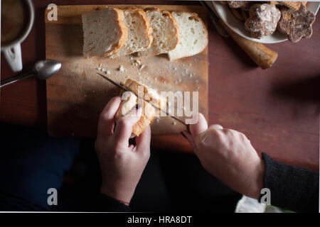 Femme coupe pain sur une vieille table en bois. focus sélectif. Lumière naturelle à partir de la fenêtre . Banque D'Images