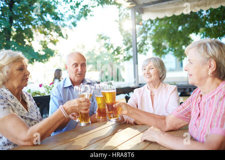 Groupe de personnes âgées à l'élégant assis dans l'air extérieur et pub qui retentit verres ensemble avec joie Banque D'Images
