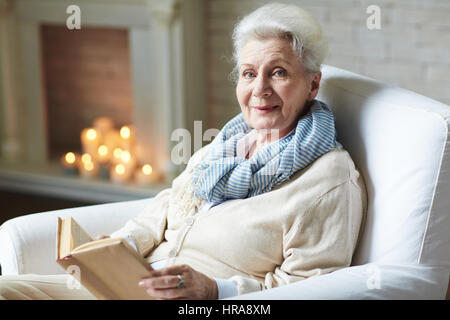 Portrait of smiling attractive woman retraités en beige cardigan distrait pour deuxième lecture du livre afin de poser pour la photographie Banque D'Images