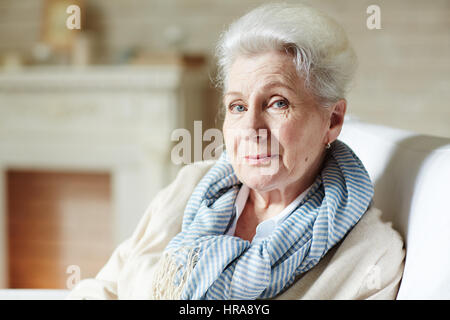 Portrait de vieille femme élégante avec le maquillage naturel foulard rayé et assis dans un fauteuil et regardant pensivement l'appareil photo Banque D'Images