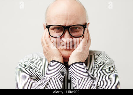 Portrait d'homme d'âge charmant dans les lunettes et chemise rayée faire drôle de visage par devenir spongieuses joues avec ses mains Banque D'Images