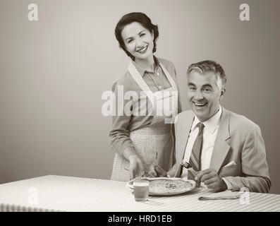 Happy vintage couple having dinner, elle est au service d'une pizza à son mari Banque D'Images