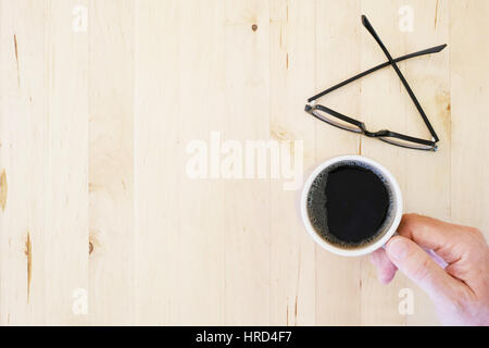 Hand Reaching for coffee mug, les lunettes sur la table en bois. Vue d'en haut. Banque D'Images