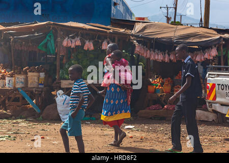 Nairobi, Kenya - 07 juillet 2013 une femme se promène le long de la rue et est titulaire à l'arrière de l'enfant, les gens au Kenya Banque D'Images