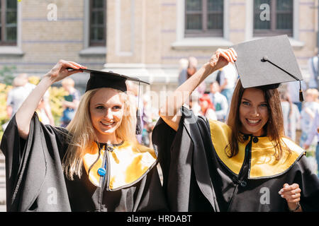 Riga, Lettonie - 1 juillet 2016 : Deux jeunes femmes diplômées de l'Université de Lettonie habillé en robe de chambre et les diplômés universitaires Square caps qui pose pour la photo Banque D'Images