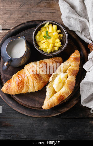 Le petit-déjeuner avec deux croissant, beurre, crème et de tranches de mangues, servi sur le bois servant à bord Rond de serviette textile sur fond de bois ancien. Banque D'Images