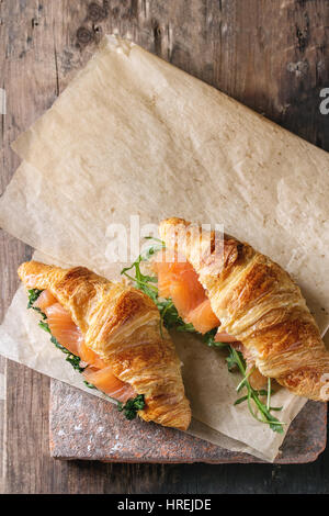 Deux croissants avec du saumon salé, fumé et à la roquette épinard servi sur du papier sulfurisé conseil terre cuite ancienne en bois foncé sur arrière-plan. Vue supérieure avec sp Banque D'Images