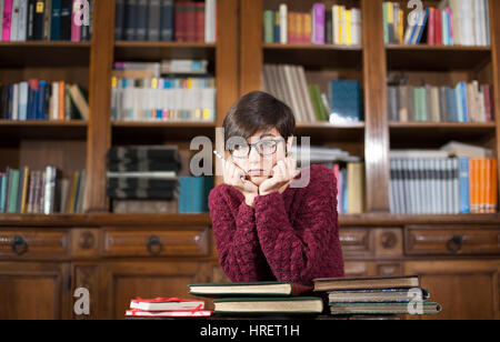 Jeune étudiante avec visage fatigué expression looking at camera avec beaucoup de livres autour de la bibliothèque Banque D'Images