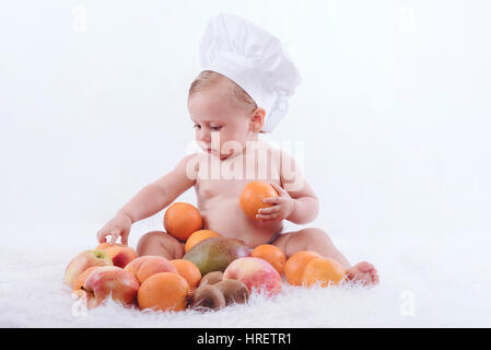 Peu heureux bébé dans un chapeau de chef avec des fruits Banque D'Images