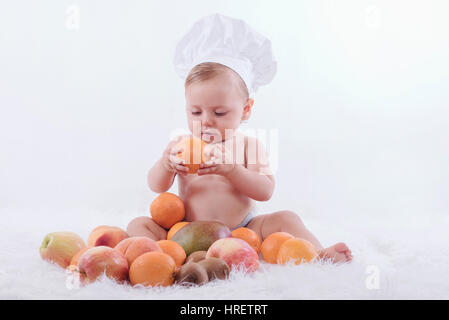 Peu heureux bébé dans un chapeau de chef avec des fruits Banque D'Images