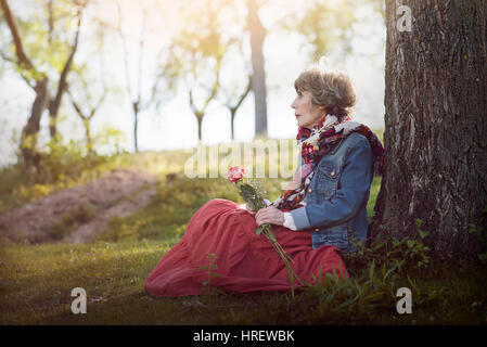 Pensive senior woman sitting on the grass. senior woman avec une rose dans sa main Banque D'Images