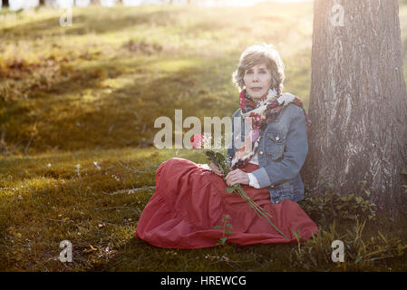 Happy senior femme assise sur l'herbe. Senior woman avec une rose dans sa main Banque D'Images