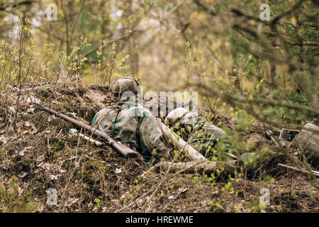 Deux inconnus de reconstitution historique habillés en soldats d'infanterie de la Wehrmacht durant la Seconde Guerre mondiale, assis avec arme fusil caché dans une embuscade dans la région de tranchée Banque D'Images