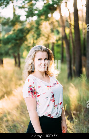 Portrait de jeunes assez grande taille Caucasian Happy Smiling Girl femme aux yeux bleus, de longs cheveux bruns ondulés en T-Shirt blanc sur la forêt d'été Backgroun Banque D'Images