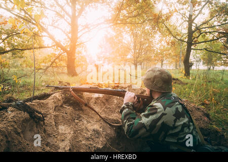 La reconstitution médiévale non identifiés habillé en soldat d'infanterie de la Wehrmacht allemande dans la seconde guerre mondiale, assis avec arme fusil caché dans une embuscade dans la tranchée à l'automne Banque D'Images