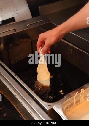 Abaisser un morceau de morue enrobés d'une pâte mélange dans une friteuse. Banque D'Images