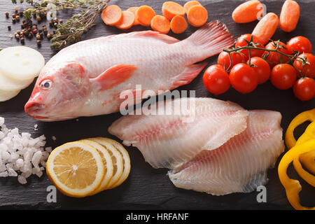 Tilapia aux légumes crus et les ingrédients, les épices close-up sur la carte Vue de dessus horizontale. Banque D'Images