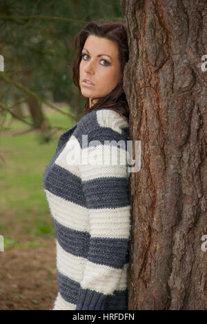 Belle jeune femme portant un cavalier dans le parc par un arbre Banque D'Images