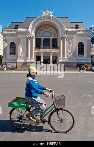 Théâtre Municipal à Ho Chi Minh Ville avec une femme du comté de conduite passé sur un bycycle lors d'une journée ensoleillée avec ciel bleu. Banque D'Images