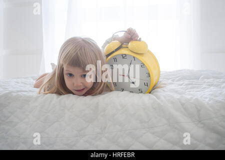 Close-up portrait of funny little girl avec un énorme réveil jaune sur fond blanc Banque D'Images