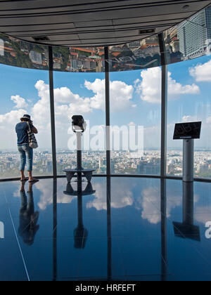 Un touriste à la recherche de la vue depuis le Saigon Skydeck dans la Bitexco Financial Tower sur une journée ensoleillée avec ciel bleu. Banque D'Images