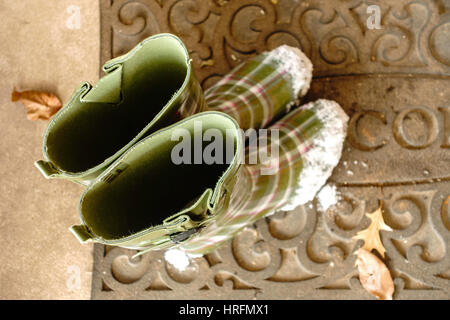 La femme vert à motifs, ou des bottes en caoutchouc, bottes de neige sur les orteils. Sur un tapis de bienvenue à l'extérieur d'une maison. Banque D'Images