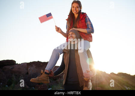 Portrait of young tourist couple célébrant la liberté américaine : belle fille de randonnées trachants assis sur ses petits amis les épaules en souriant était enjoué Banque D'Images