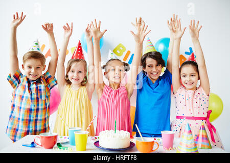 Groupe de cinq enfants sourire joyeux permanent de couleurs vives dans une rangée à côté de la table d'anniversaire avec gâteau sur elle jusqu'holding hands Banque D'Images