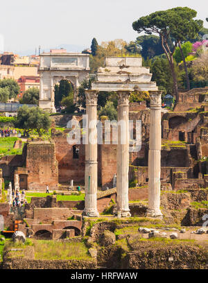 Rome, Italie. Le Forum Romain. Les trois colonnes du Temple de Castor et Pollux. L'Arc de Titus à l'arrière-plan. Le Forum est une partie de l'Hi Banque D'Images