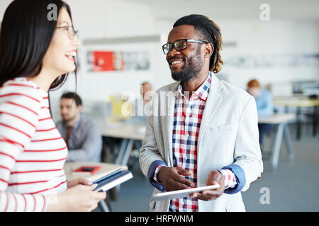 Les collègues masculins et féminins en permanent open plan office et rire de quelque chose, Afro-employé holding digital tablet in hands Banque D'Images