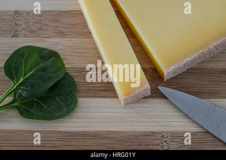 Tranche de fromage comte français sur une planche à découper en bois avec des feuilles d'épinards frais vert closeup Banque D'Images