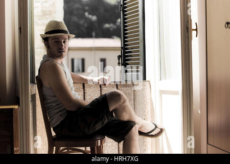 Parution du modèle, Junger Mann mit Hut sitzt am offenen Fenster - homme avec chapeau à côté de la fenêtre Banque D'Images