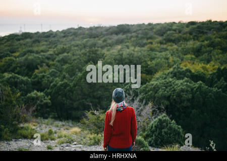 Young blonde woman in gray hat et red sweater attend avec intérêt sur le fond de la forêt. woman enjoying view. Banque D'Images