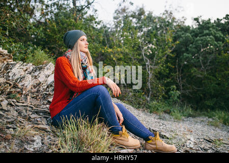 Portrait d'une belle jeune femme blonde avec chapeau, pull rouge, bleu jeans et bottes jaunes se trouve en plein air, sur l'arrière-plan de l'aménagement forestier Banque D'Images