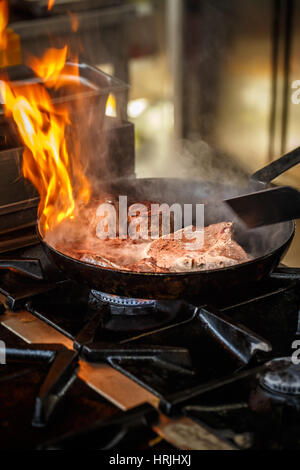 Chef de friture dans flaming pan sur une cuisinière à gaz dans la cuisine commerciale. Banque D'Images