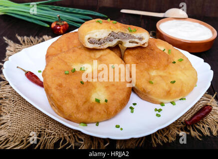 Faites frire les tartes à la viande sur une plaque blanche avec de la crème sur fond de bois sombre. Banque D'Images
