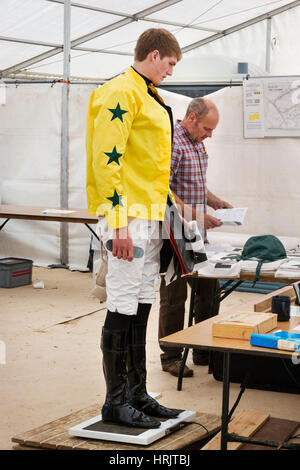 Jockey dans une chemise jaune debout sur l'échelle de pesage, la pesée avant une course de chevaux. Banque D'Images