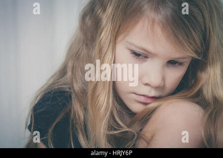 Portrait de triste petite fille assise près de la fenêtre à la maison au moment de la journée Banque D'Images