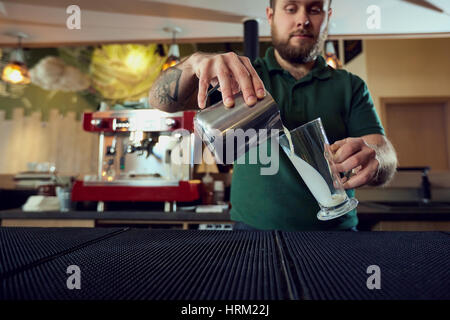 Le barman, barista verse le lait chaud dans un verre dans bar café Banque D'Images