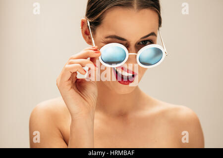 Portrait de belle jeune femme avec des lunettes. Modèle de mode féminine avec des lunettes clin contre fond beige. Banque D'Images