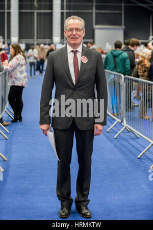 Candidat du Sinn Fein Gerry Kelly au centre principal de comptage de Belfast Titanic, Centre d'exposition, alors que le personnel électoral count count bulletins au cours de l'Assemblée générale des élections. Banque D'Images