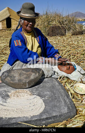 Femme indienne Uros Maïs Broyage sur île flottante faites de roseaux tortora, Puno, Lac Titicaca, Pérou Banque D'Images