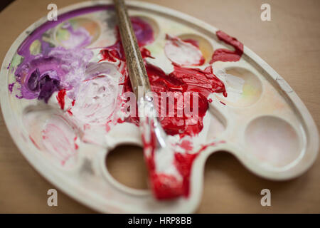 Enduit avec le pinceau de la palette avec les peintures. Peinture rouge et violet Banque D'Images
