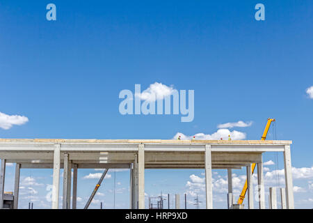 Vue sur site de construction, béton inachevé édifice haut avec les travailleurs sur le dessus. Banque D'Images