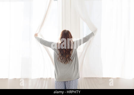 La femme ouvre les rideaux tôt le matin, vue arrière Banque D'Images